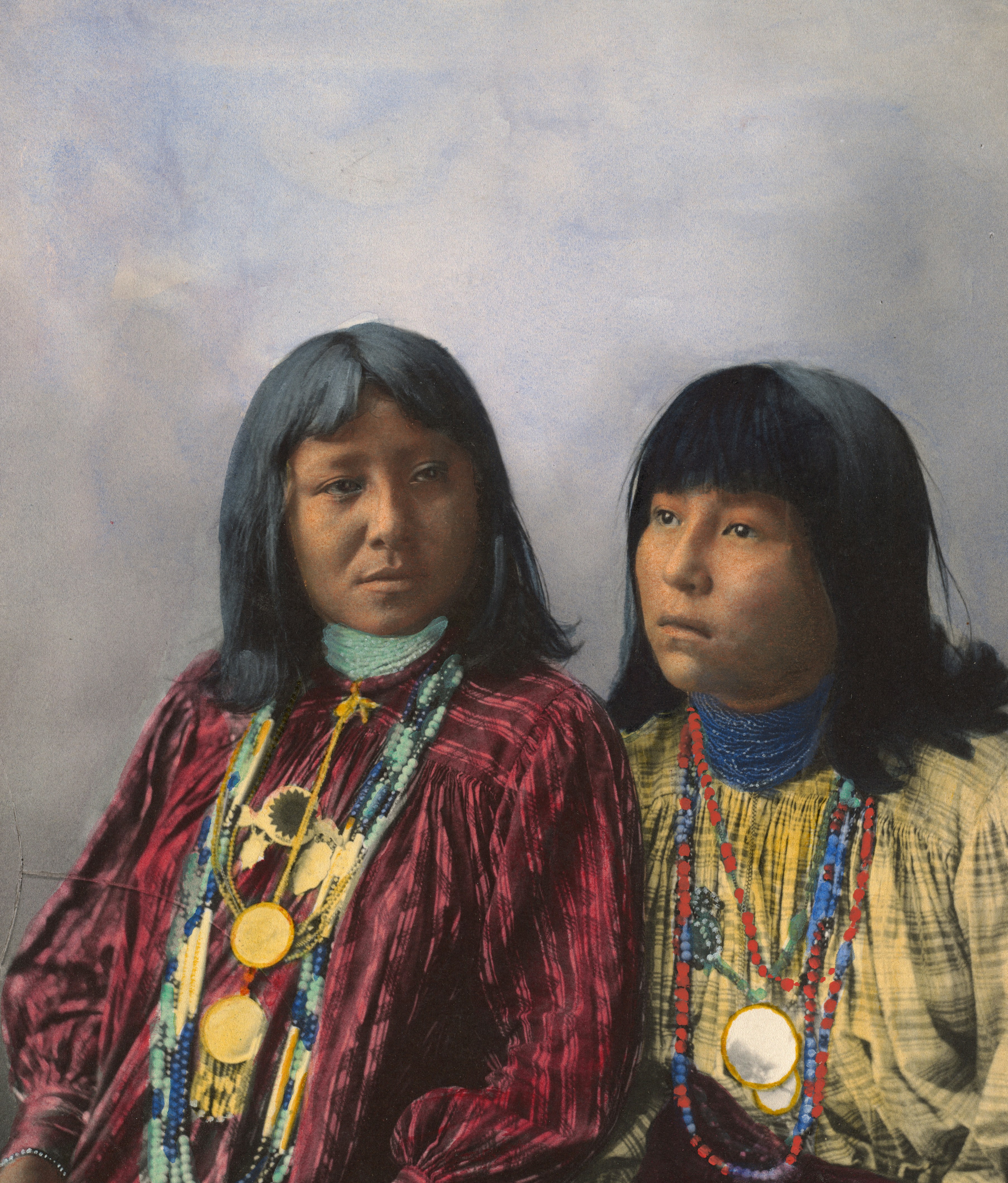 A hand-tinted portrait of two young people standing close together, each wearing several layered beaded necklaces over a patterned blouse, one red and one yellow.